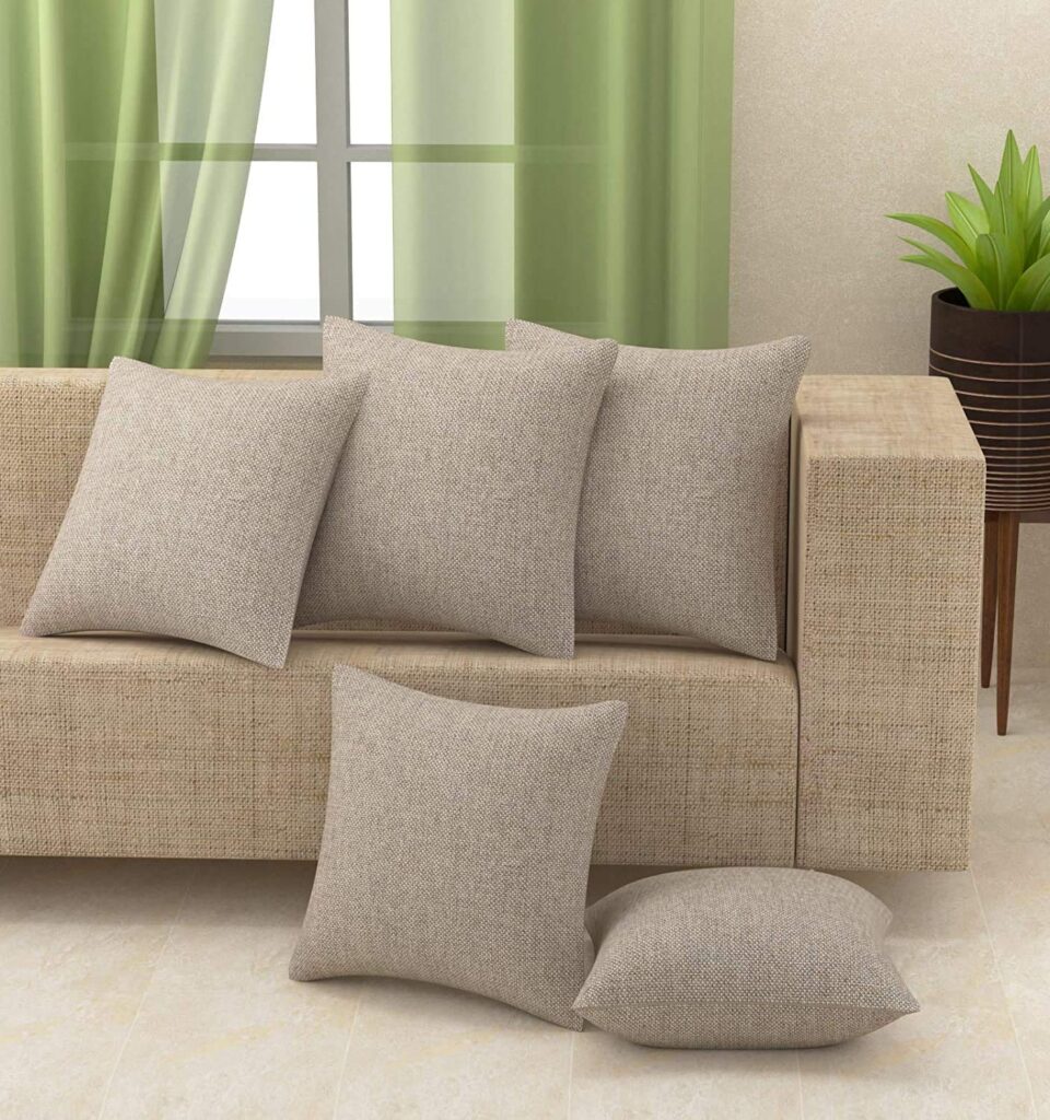 Beige cushion covers on a sofa with matching throw pillows, modern living room decor with green curtains and indoor plant